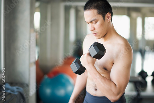 Young Asian man exercising with dumbbells and looking at the dumbbells in the gym. man workout at fitness room. man losing weight training. © linghaa