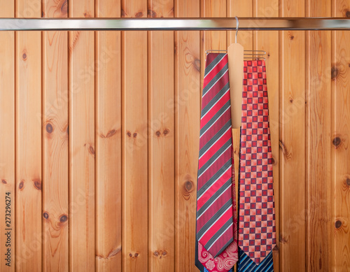 Many mens ties hanging on the rack. Wooden background.
