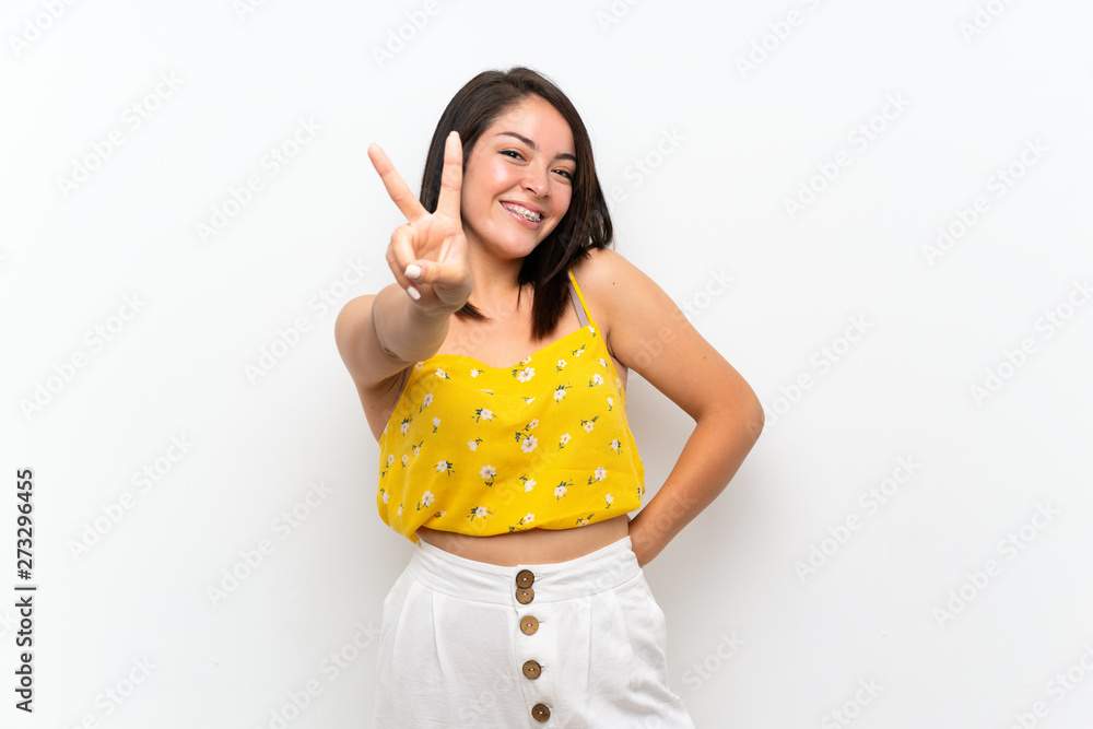 Young Mexican woman over isolated wall smiling and showing victory sign Young Mexican woman over isolated wall smiling and showing victory sign