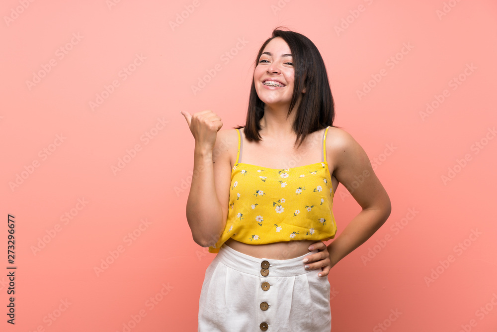 Young Mexican woman over isolated wall pointing to the side to present a product Young Mexican woman over isolated wall pointing to the side to present a product
