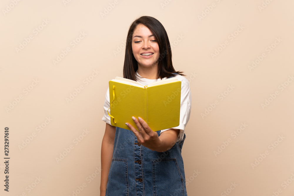 Young Mexican woman over isolated background holding and reading a book Young Mexican woman over isolated background holding and reading a book