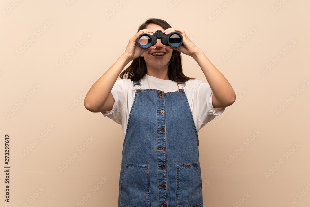 Young Mexican woman over isolated background with black binoculars