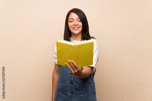 Young Mexican woman over isolated background holding and reading a book