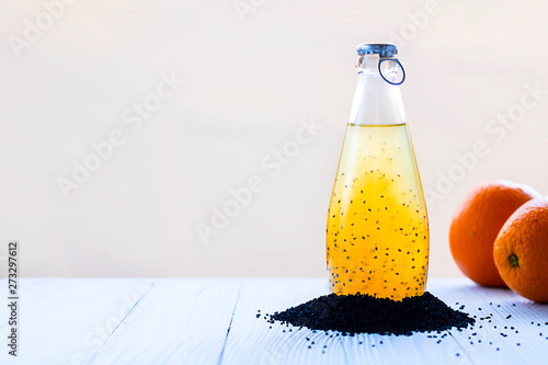 Colorful summer drink with basil seeds in bottle with blue cap surraounded with black basilica grains and defocused orange on background Horizontal copy space Healthy beverage, superfood, detox, vegan photo