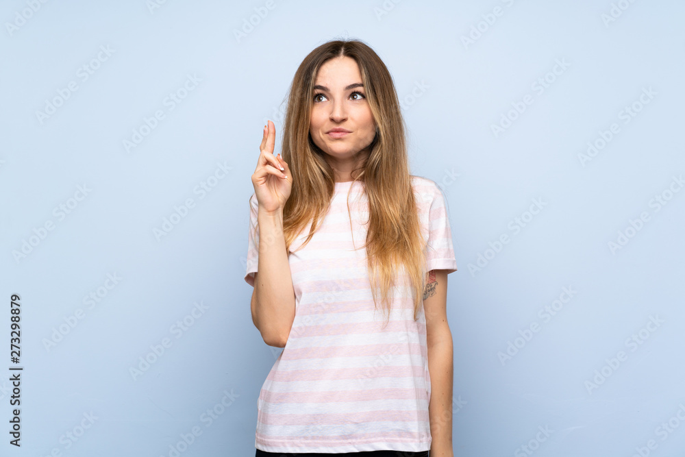 Young woman over isolated blue background with fingers crossing and wishing the best Young woman over isolated blue background with fingers crossing and wishing the best