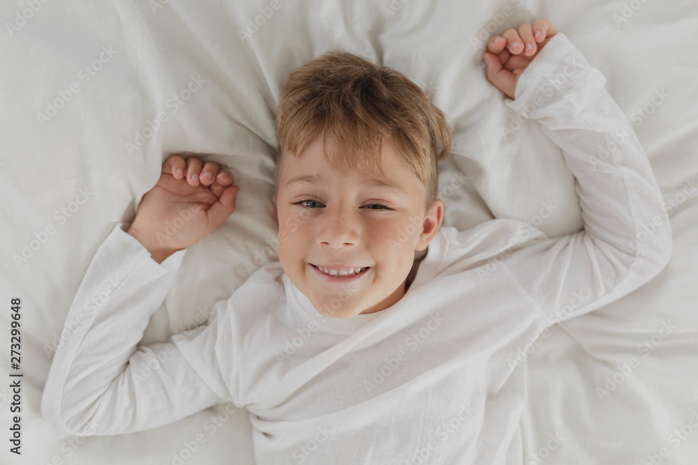 Cute boy looking at camera while lying on bed in bedroom at comfortable home Cute boy looking at camera while lying on bed in bedroom at comfortable home
