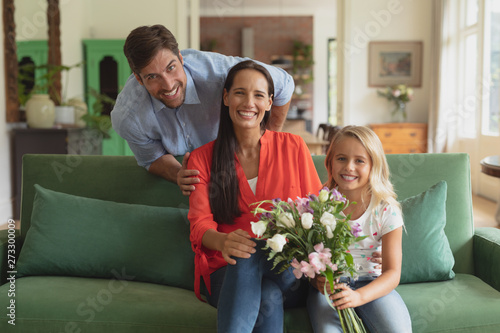Family with flower bouquet sitting on sofa in living room at home