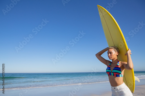 Beautiful woman in bikini carrying the surfboard on her head at beach in the sunshine