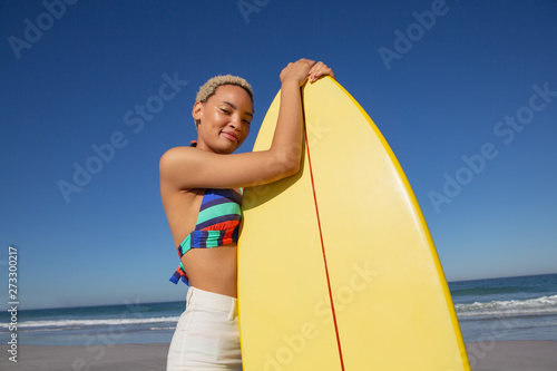 Beautiful woman in bikini standing with surfboard on beach in the sunshine