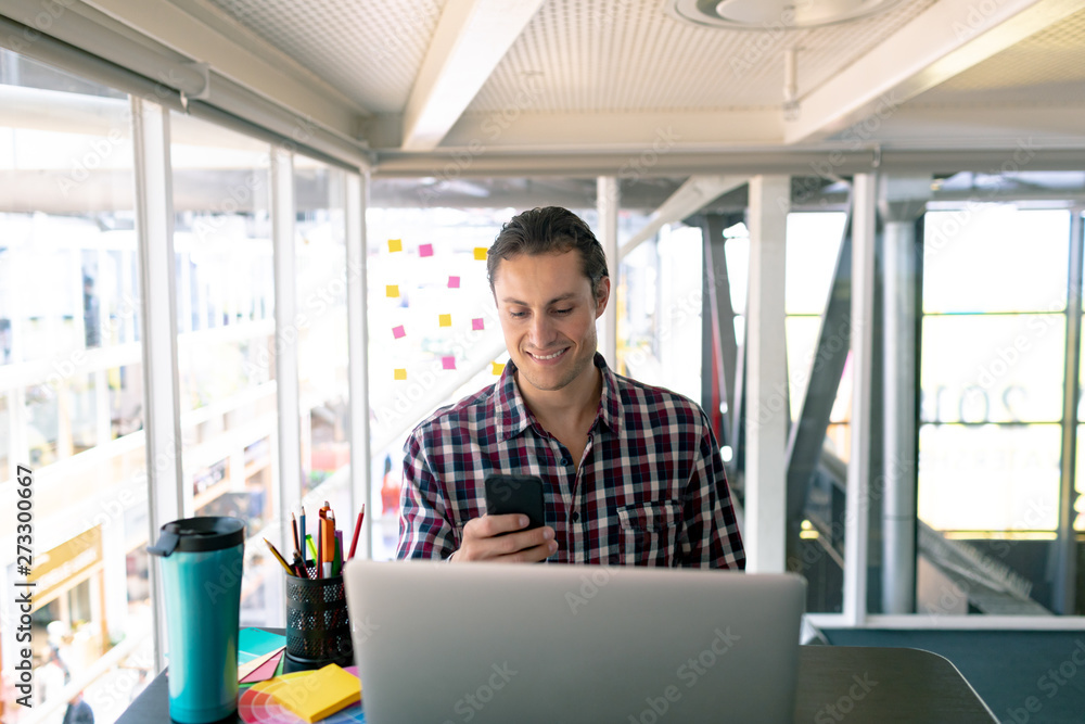 Fototapeta premium Male graphic designer using mobile phone while working on laptop at desk