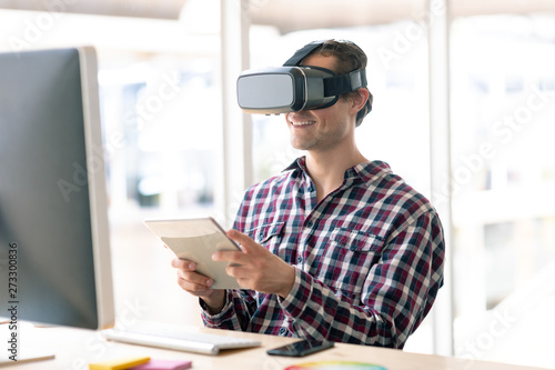 Male graphic designer using virtual reality headset while working on digital tablet at desk