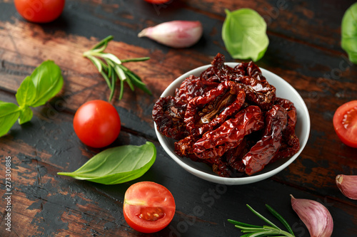 Sun dried tomatoes in white bowl with fresh herbs and spices on wooden table