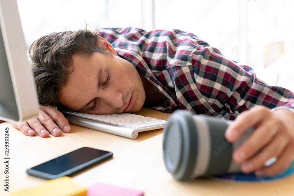 Male graphic designer sleeping on desk in a modern office Male graphic designer sleeping on desk in a modern office