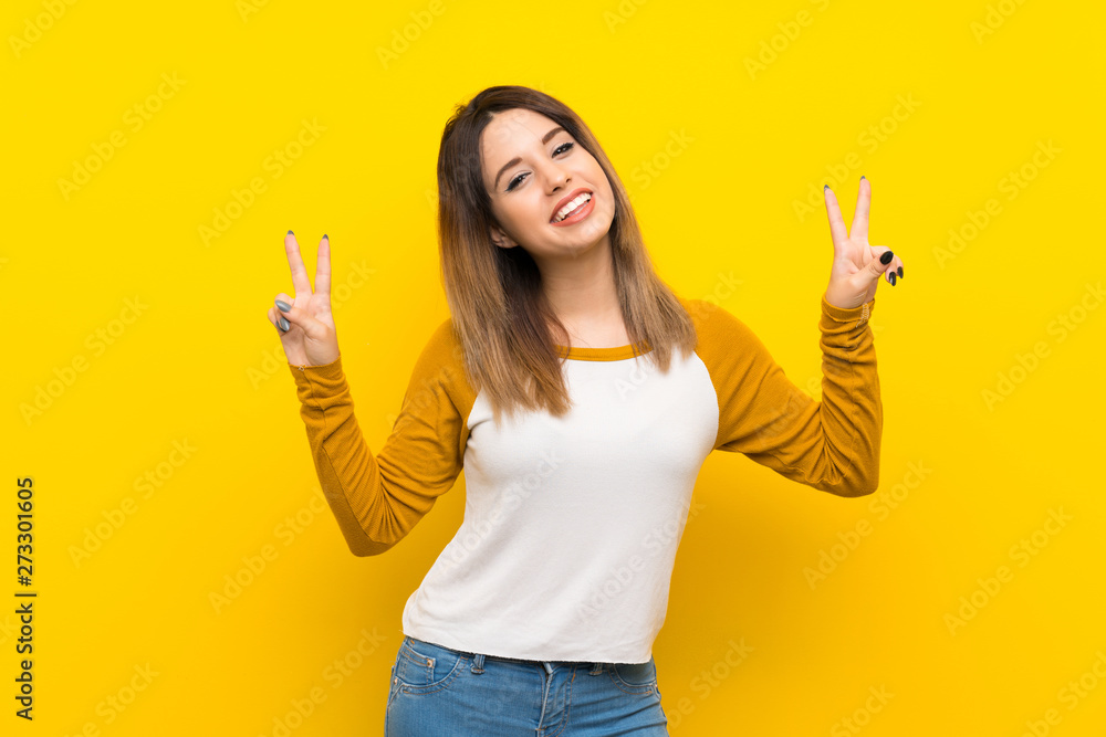 Pretty young woman over isolated yellow wall showing victory sign with both hands Pretty young woman over isolated yellow wall showing victory sign with both hands
