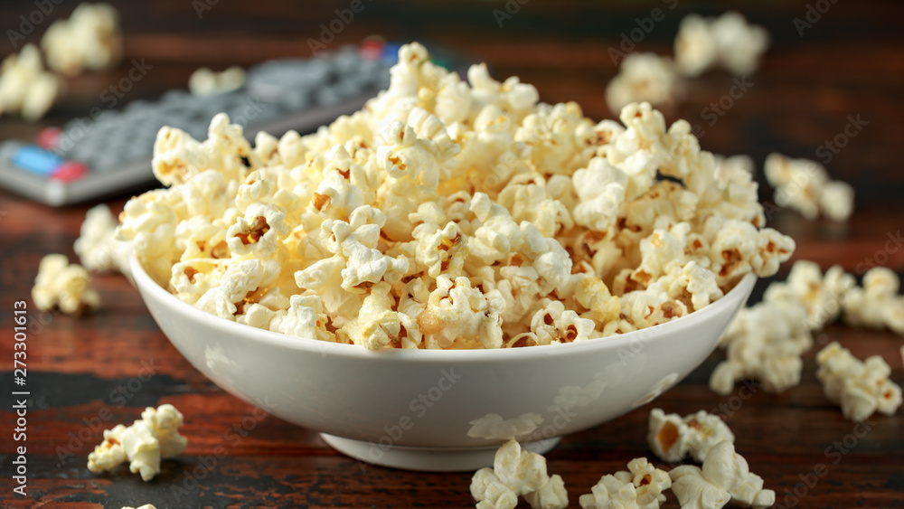 bowl of salty popcorn and remote control on wooden table bowl of salty popcorn and remote control on wooden table