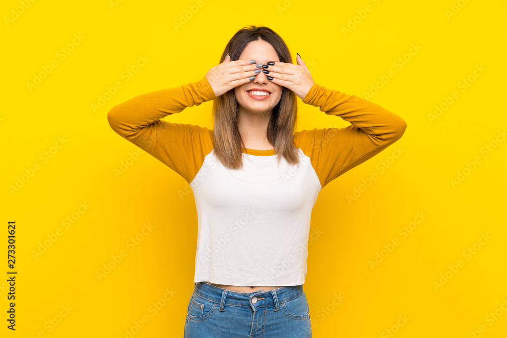 Pretty young woman over isolated yellow wall covering eyes by hands Pretty young woman over isolated yellow wall covering eyes by hands