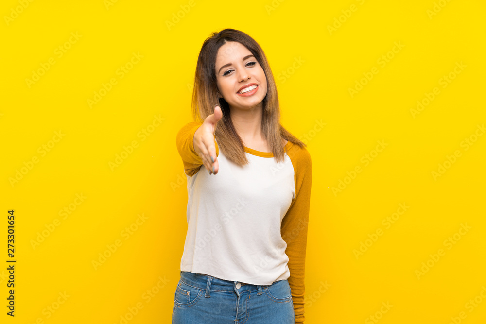 Pretty young woman over isolated yellow wall shaking hands for closing a good deal Pretty young woman over isolated yellow wall shaking hands for closing a good deal