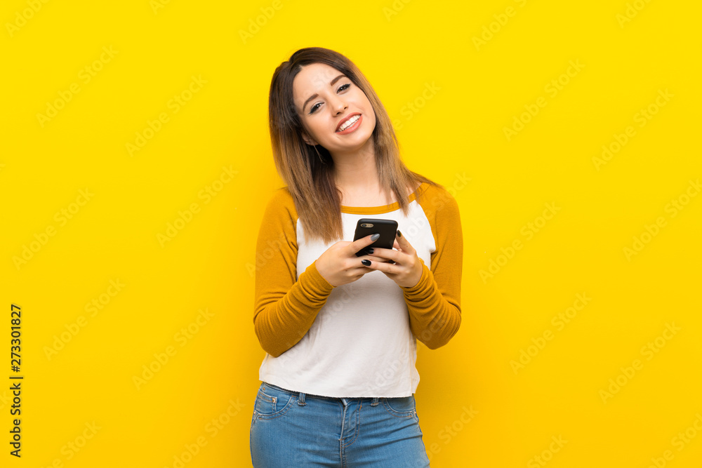 Pretty young woman over isolated yellow wall sending a message with the mobile Pretty young woman over isolated yellow wall sending a message with the mobile
