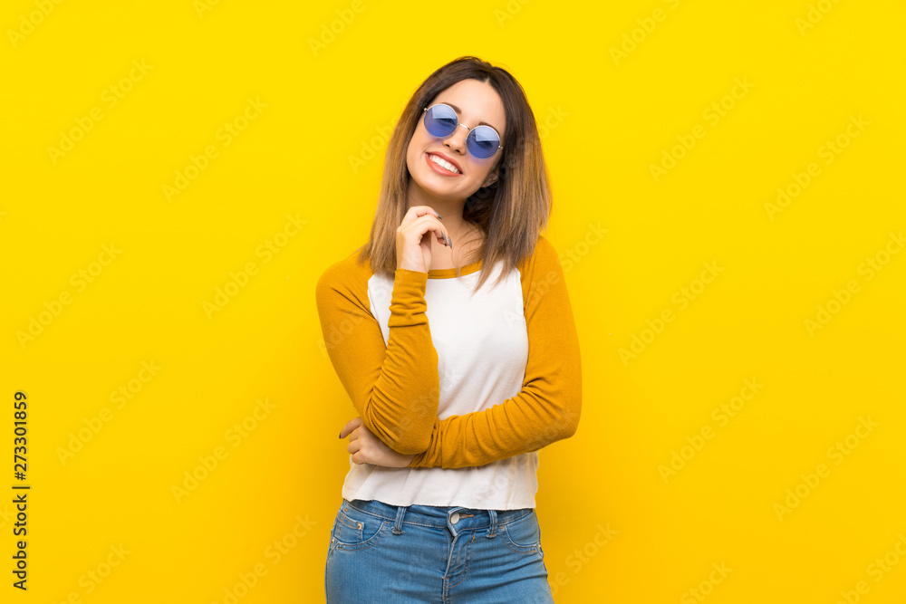 Pretty young woman over isolated yellow wall with glasses and smiling Pretty young woman over isolated yellow wall with glasses and smiling