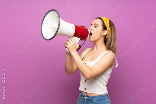 Pretty young woman over isolated purple wall shouting through a megaphone