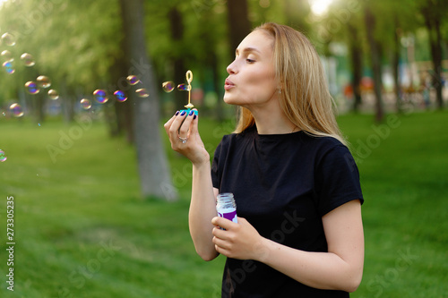 Young beautiful girl inflates soap bubbles in the summer sunny park