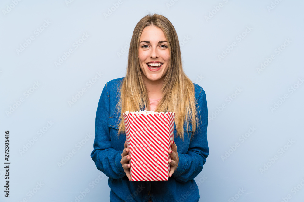 Happy blonde woman with popcorns over blue wall Happy blonde woman with popcorns over blue wall