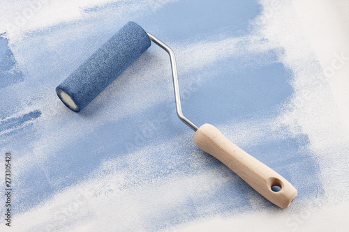 Sponge roller with blue paint on white wallpaper background