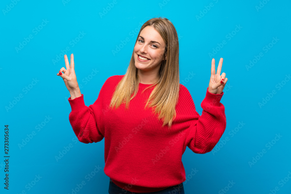 Woman with red sweater over blue wall showing victory sign with both hands Woman with red sweater over blue wall showing victory sign with both hands