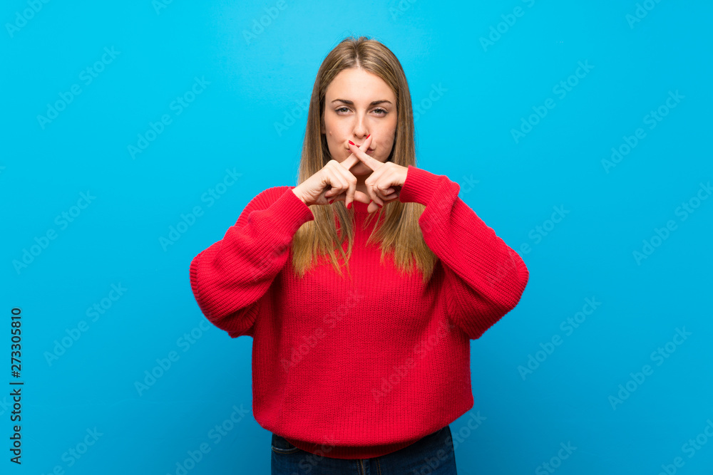 Woman with red sweater over blue wall showing a sign of silence gesture Woman with red sweater over blue wall showing a sign of silence gesture
