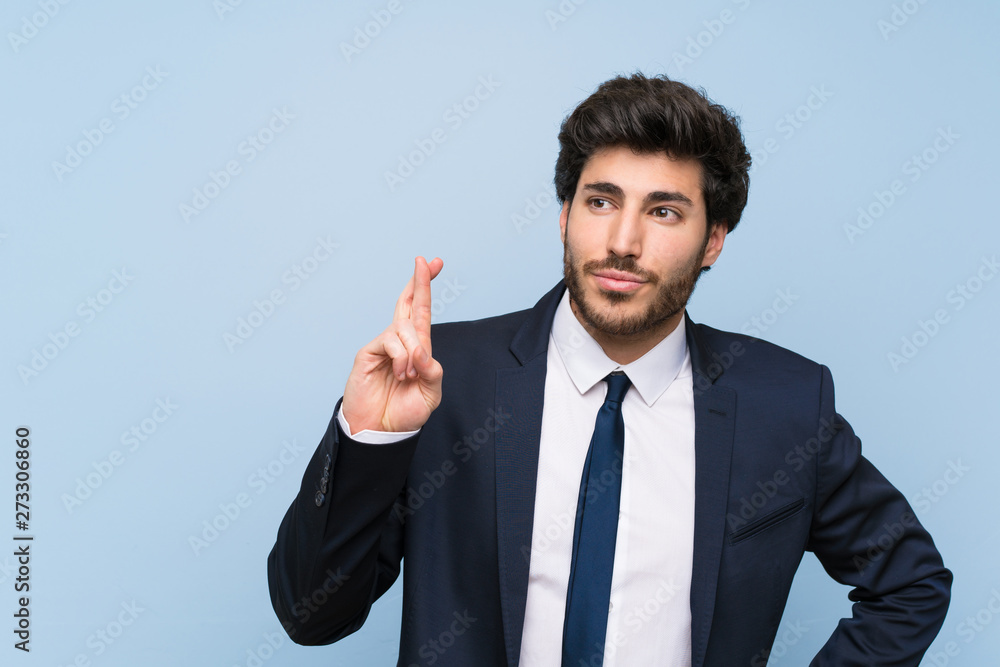 Businessman over isolated blue wall with fingers crossing and wishing the best Businessman over isolated blue wall with fingers crossing and wishing the best
