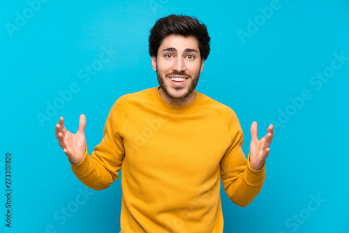 Handsome over isolated blue wall with shocked facial expression
