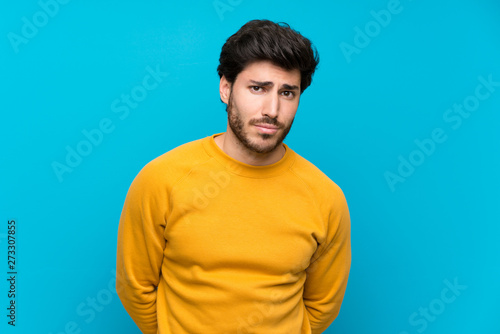 Handsome over isolated blue wall with sad and depressed expression
