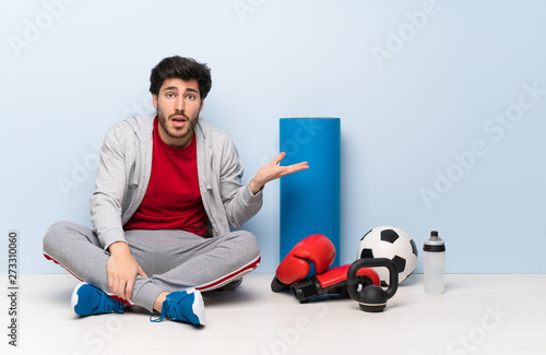 Sport man sitting on the floor making doubts gesture