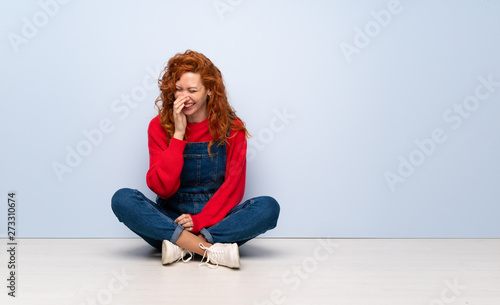Redhead woman with overalls sitting on the floor smiling a lot