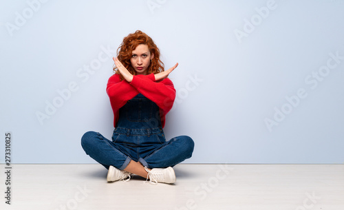 Redhead woman with overalls sitting on the floor making NO gesture