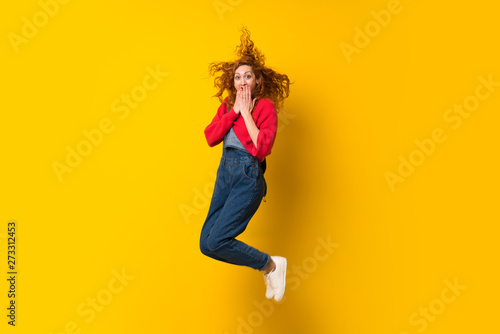 Fototapeta Naklejka Na Ścianę i Meble -  Redhead woman with overalls jumping over isolated yellow wall
