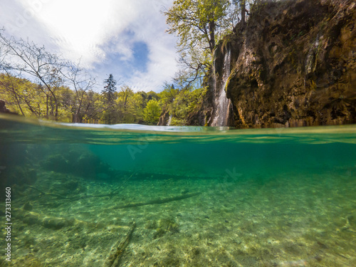 Amazing split view of lake with sunken tree trunk and waterfall in the background. Plitvice national park, Croatia.