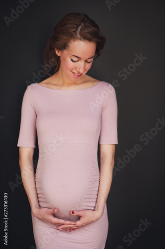 Pregnant happy Woman touching her belly. Pregnant middle aged mother portrait, caressing her belly and smiling close-up. Healthy Pregnancy concept, brunette expectant female on blue background
