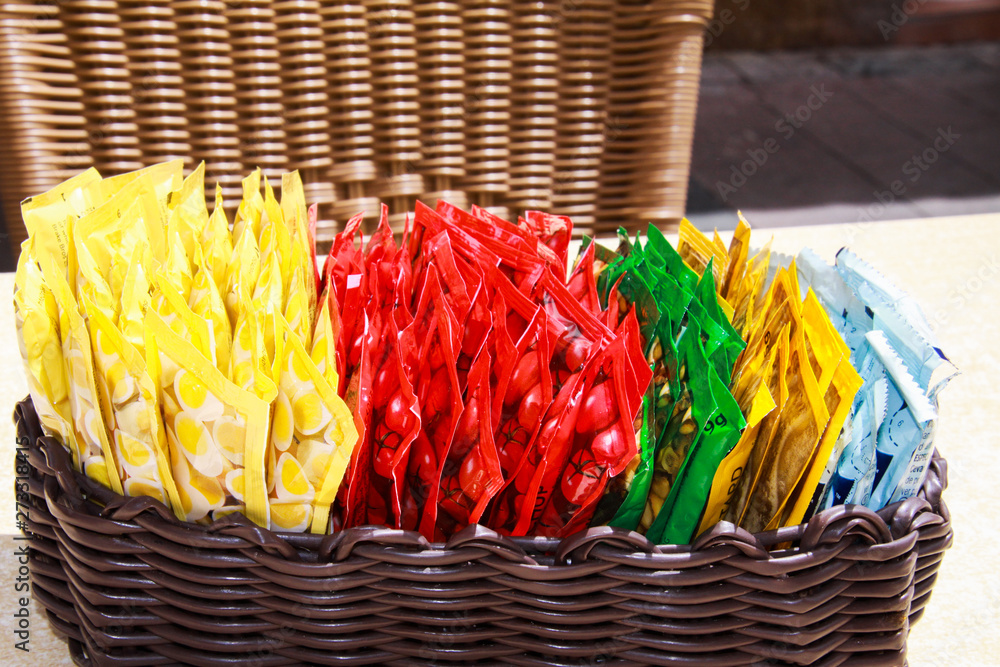 Close up of wooden basket with choice of small colorful plastic packages of sauces on table of restaurant outdoor