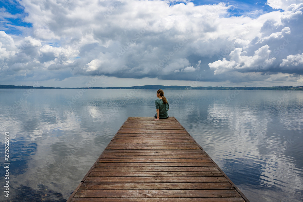 A woman is sitting alone on a wooden walkway at the Lago di Bracciano in Italy