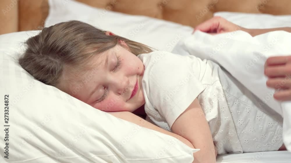 Cute little girl going to sleep in her bed, mother tucking the blanket. Cropped shot of adorable little girl smiling to the camera, falling asleep, her mom tucking her in. Love, family concept Cute little girl going to sleep in her bed, mother tucking the blanket. Cropped shot of adorable little girl smiling to the camera, falling asleep, her mom tucking her in. Love, family concept