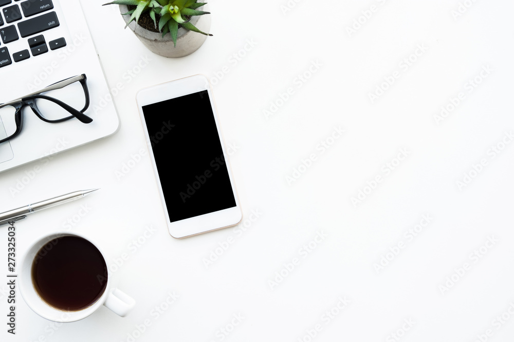White smartphone with blank mock up screen is on top white office desk table with laptop computer, cup of coffee and supplies. Top view with copy space, flat lay.