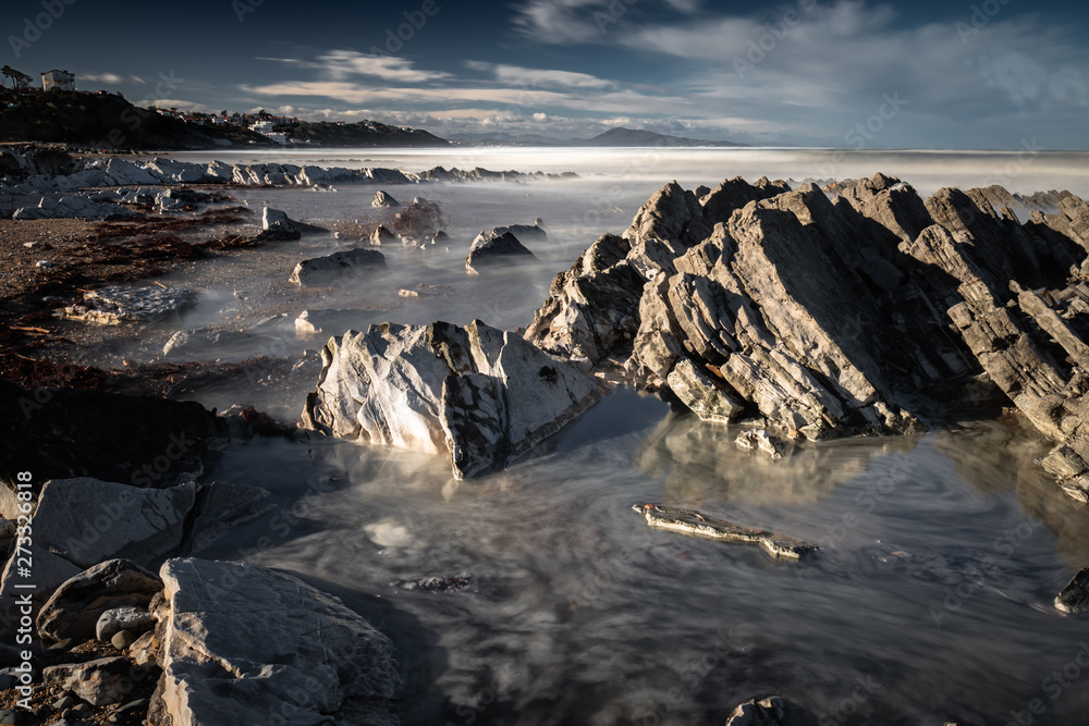 Obraz premium close up on beautiful sandy beach with rocks on atlantic coast in bidart in long exposure in beautiful sunny morning, basque country