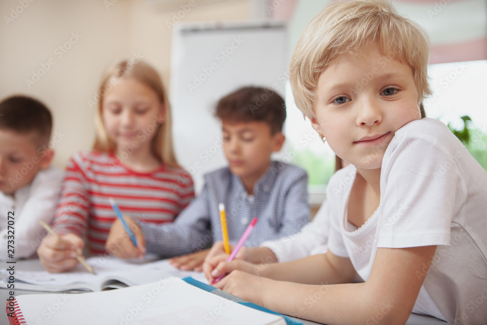 Charming little blond haired girl looking to the camera during art class, copy space. Adorable schoolgirl enjoying drawing at elementary school lesson Charming little blond haired girl looking to the camera during art class, copy space. Adorable schoolgirl enjoying drawing at elementary school lesson