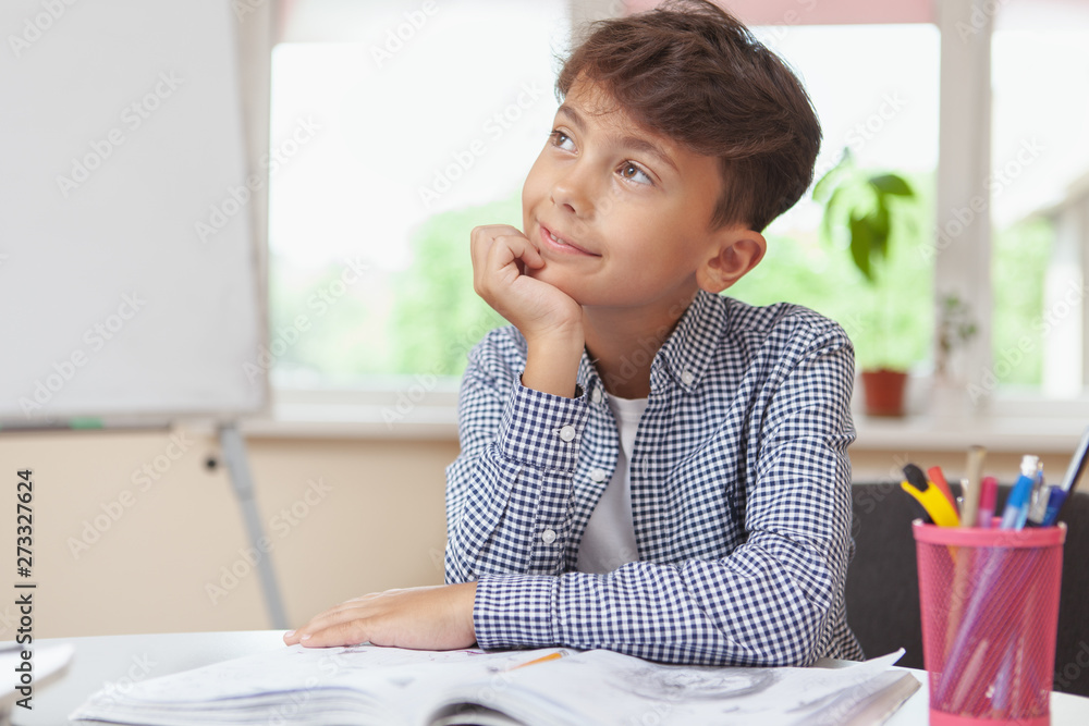 Inspiration, ideas concept. Charming young boy smiling, looking away thoughtfully sitting over his textbooks at school classroom, copy space Inspiration, ideas concept. Charming young boy smiling, looking away thoughtfully sitting over his textbooks at school classroom, copy space