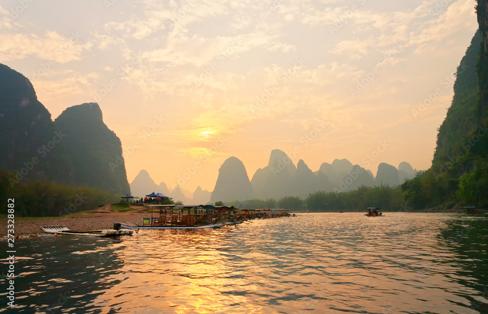 China. Yangshuo. Beautiful Li (Lijiang) River with green karst hills at sunset. Tourists travel along the river on traditional bamboo rafts and admire the setting sun in an unusual natural park - obrazy, fototapety, plakaty 