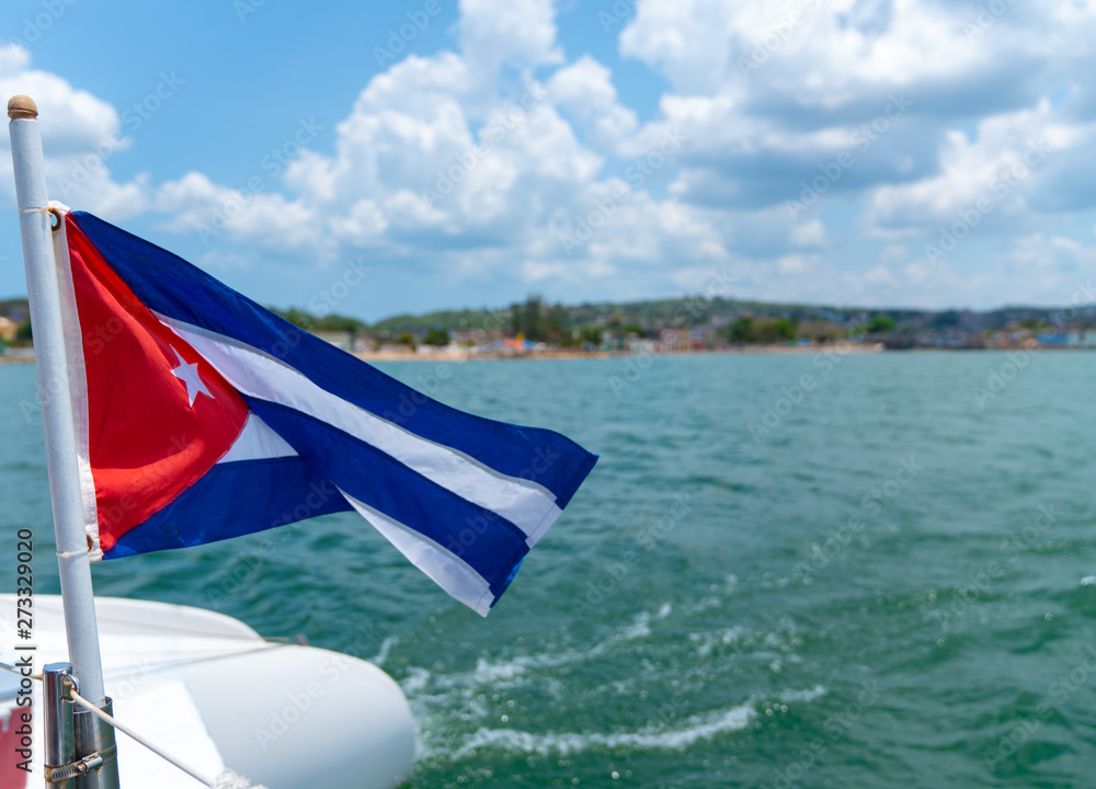 Fototapeta premium Cuba flag waving on boat at sea near Cuban coastline
