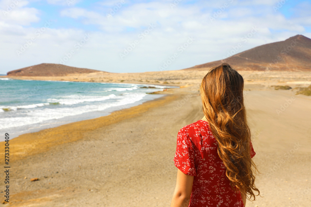 Back view of beautiful girl in red dress standing on the beach, El Medano, Tenerife Back view of beautiful girl in red dress standing on the beach, El Medano, Tenerife