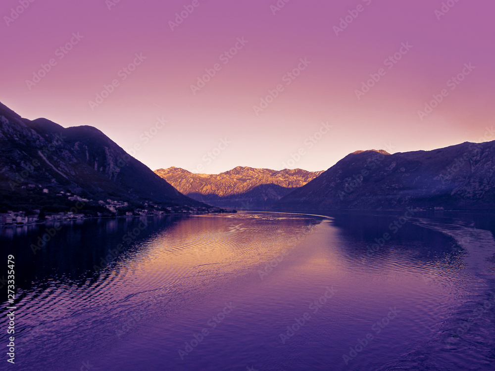 Kotor bay, Montenegro, Europe. Beautiful landscape of the sea, coastline, mountains and sky. View from a cruise ship that leaves a trail of waves on a calm water surface. 