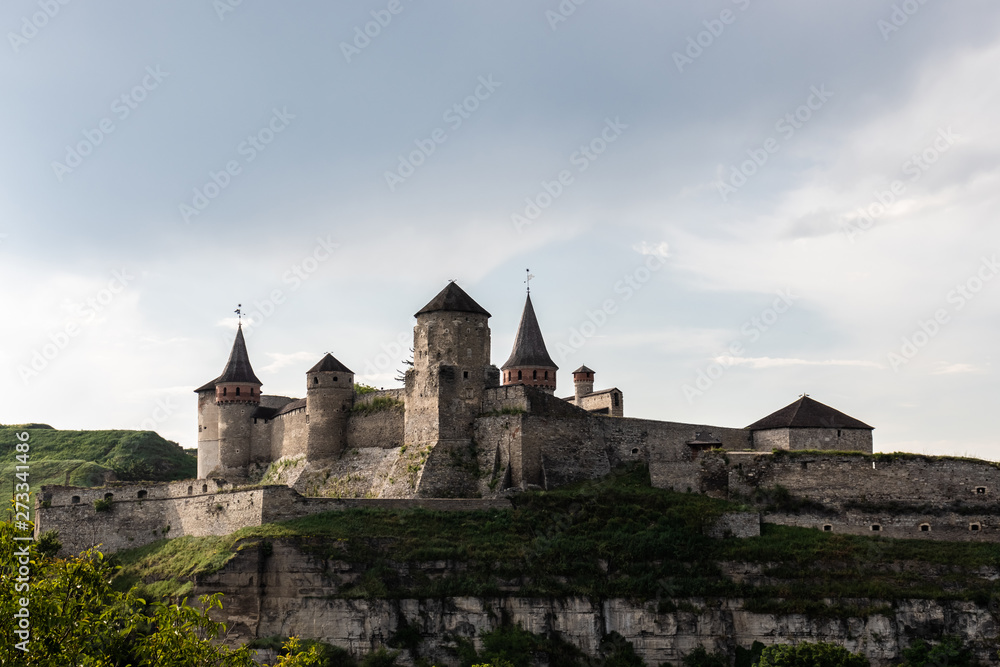 Medieval Kamianets-Podilskyi fortress of the XVI century on a rocky green hill under the evening cloudy sky. Ukraine.
